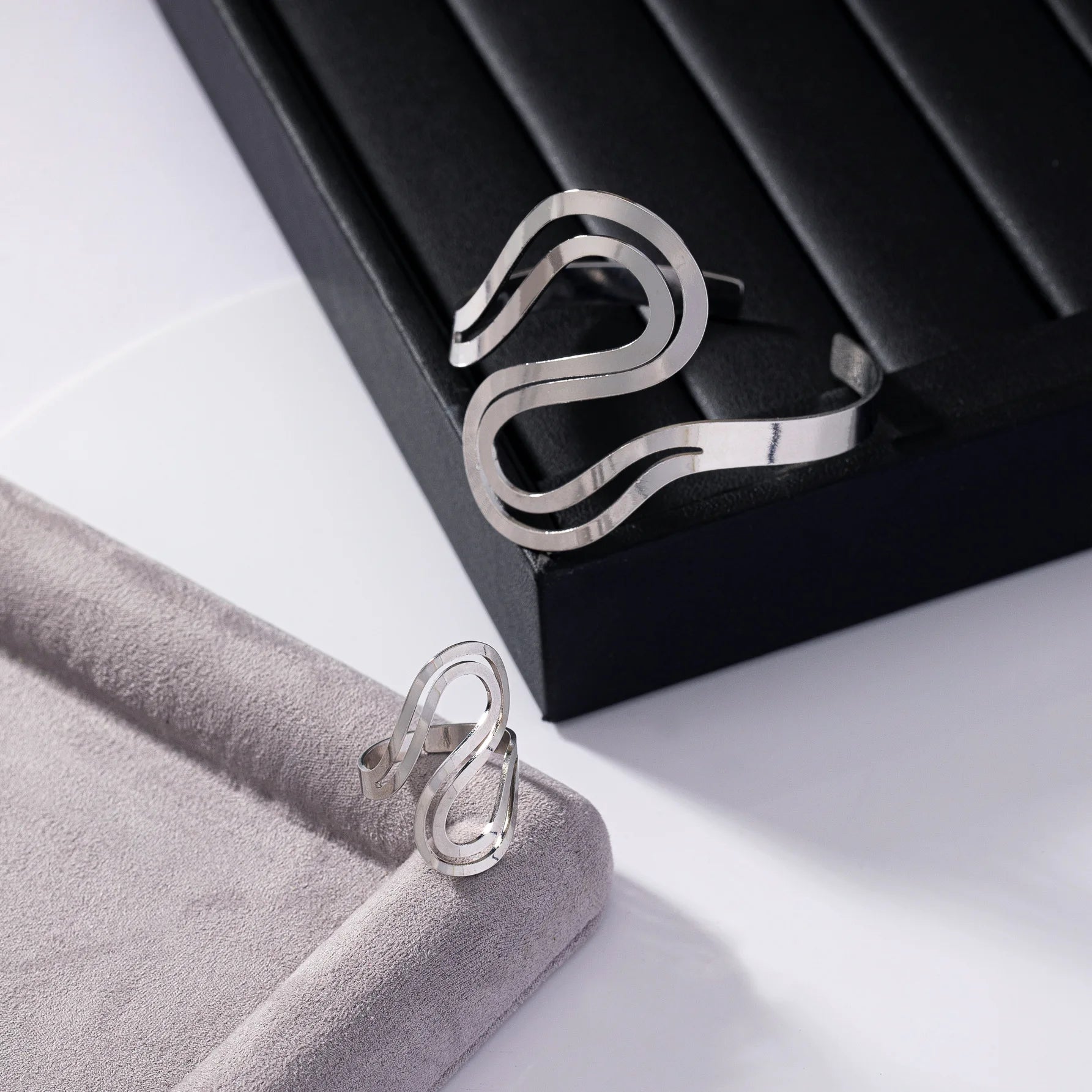 Minimalist silver snake wave bracelet and matching ring displayed on black and grey surfaces