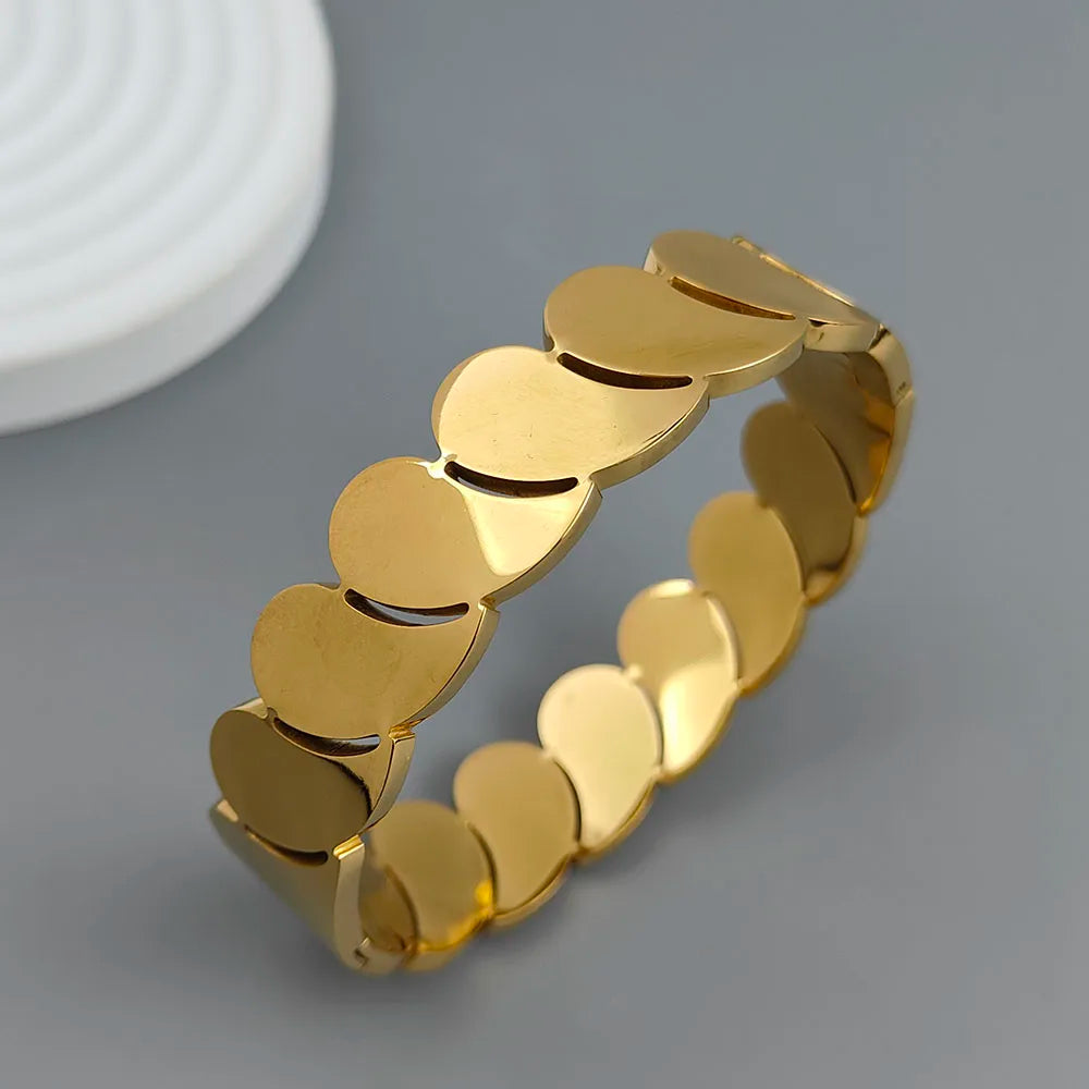 Gold cuff bracelet with polished heart-shaped links on a gray background