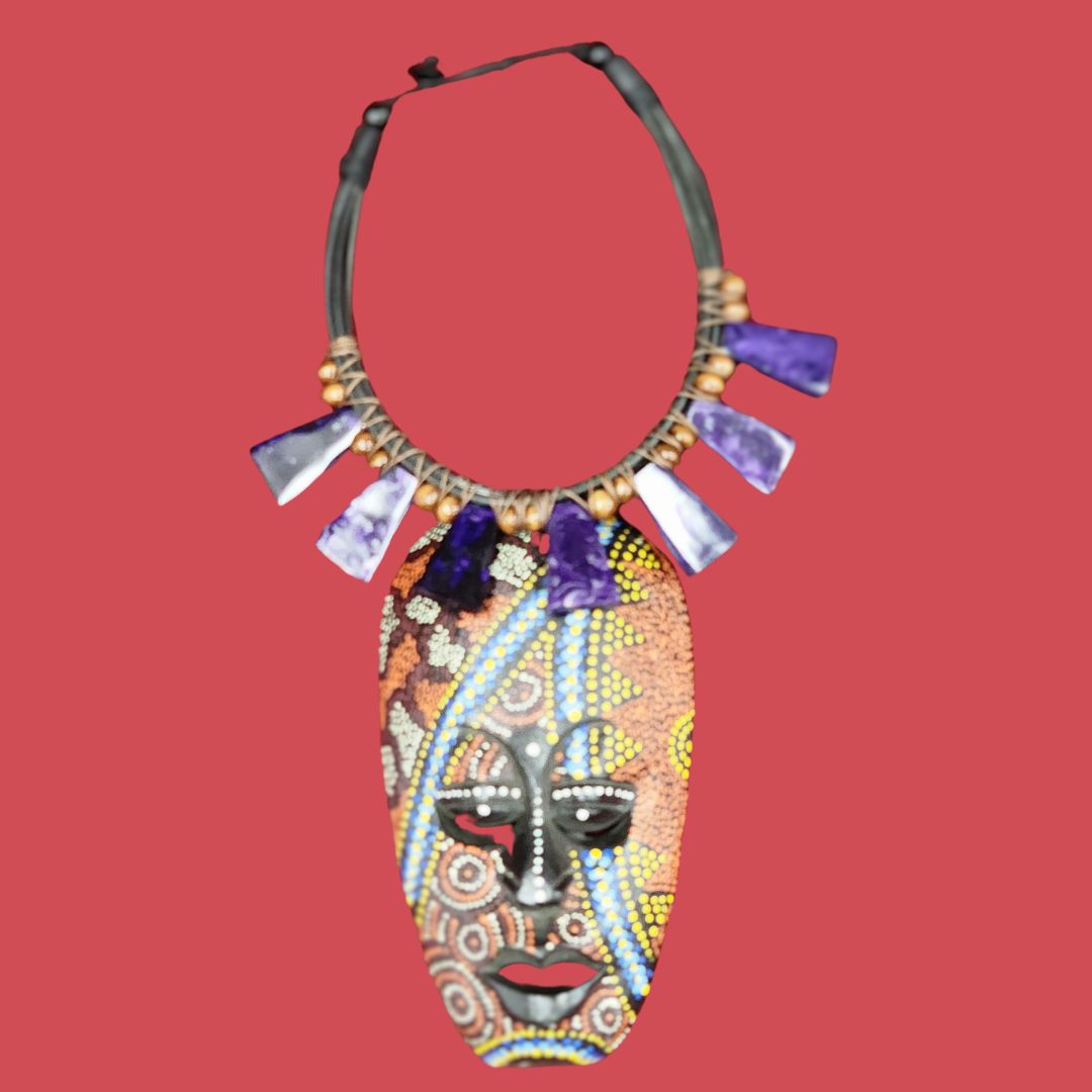 Amethyst Twilight Charm Necklace featuring a handcrafted African mask pendant with intricate beadwork and wooden beads. Accented with purple amethyst charms.
