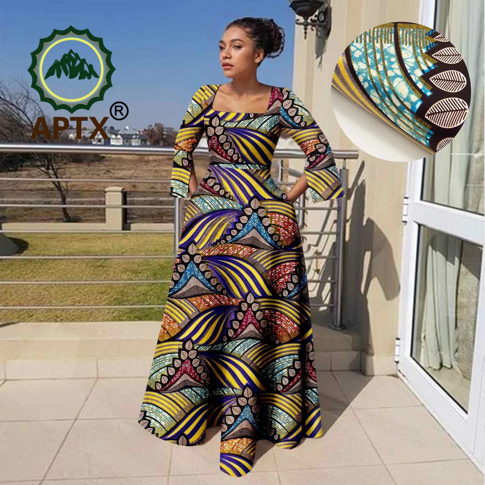 Woman in a colorful patterned dress standing outdoors with a hat on a stand.