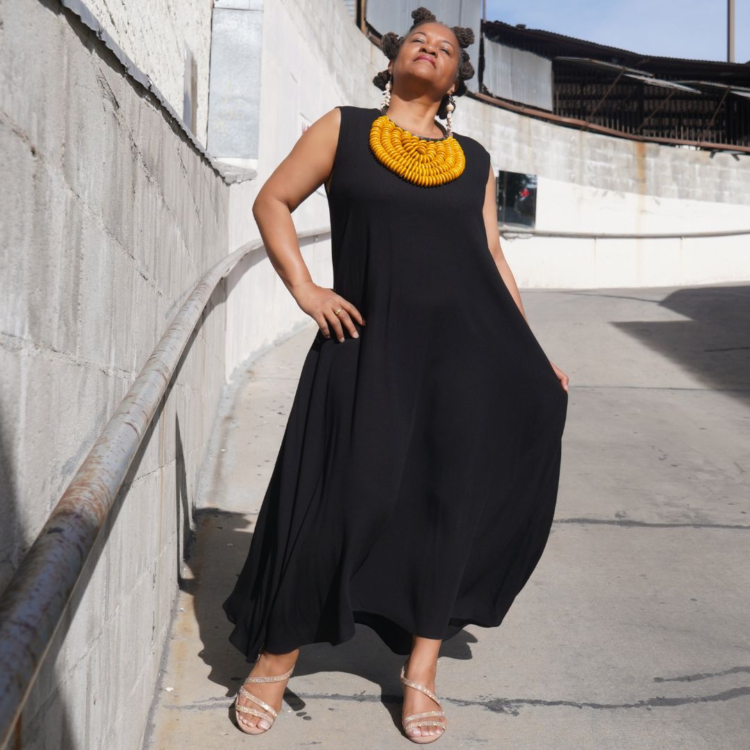 Flowy black maxi dress with pockets, accessorized with a bold yellow necklace. A perfect blend of elegance and comfort.