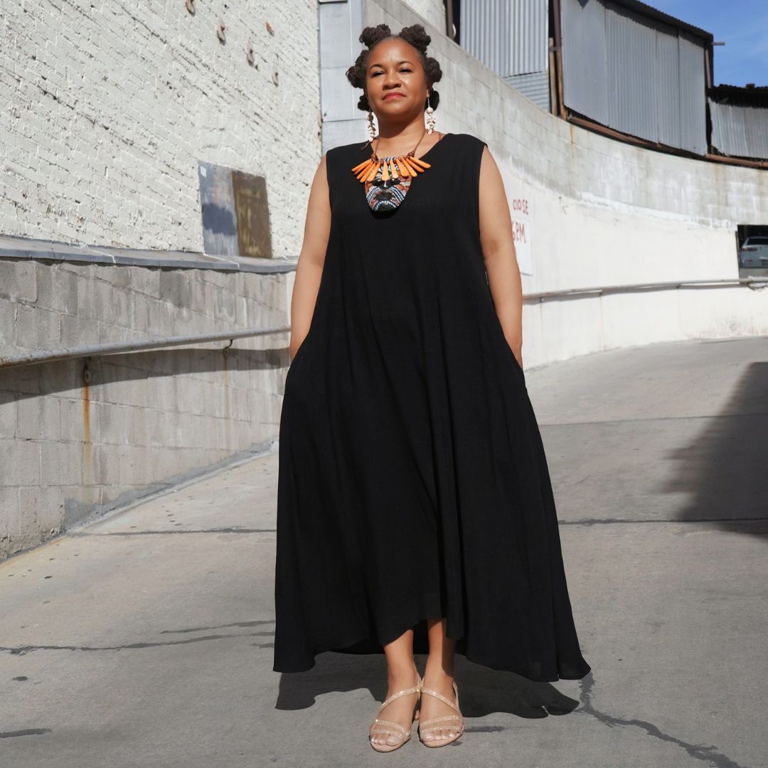 Minimalist black maxi dress with pockets, accessorized with a bold orange necklace. A timeless and elegant wardrobe staple.