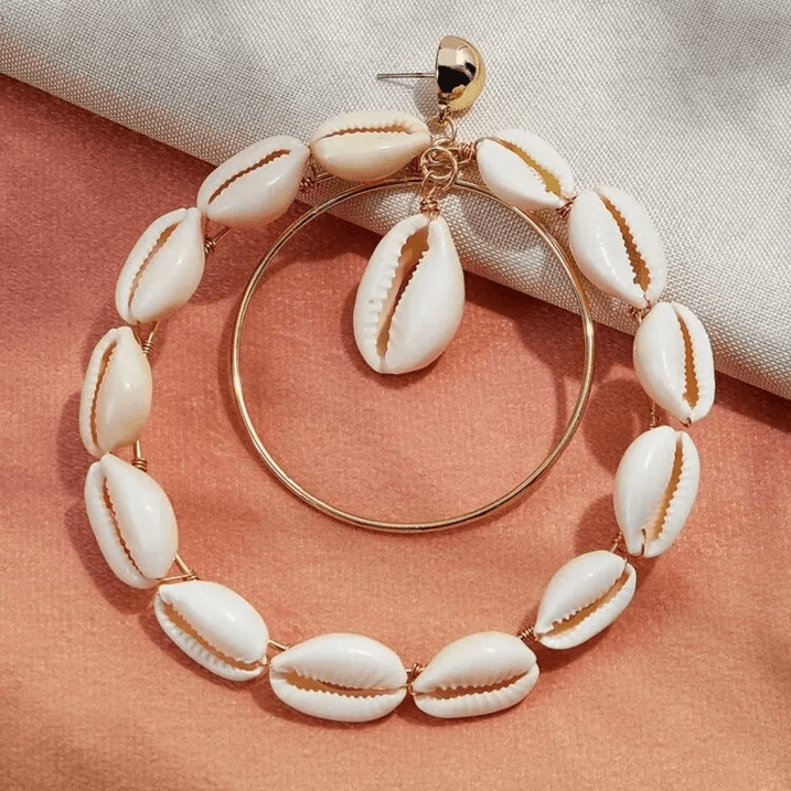 Close-up of double hoop Cowrie Shell earrings with gold-tone accents, showcasing intricate shell details on a soft fabric background.