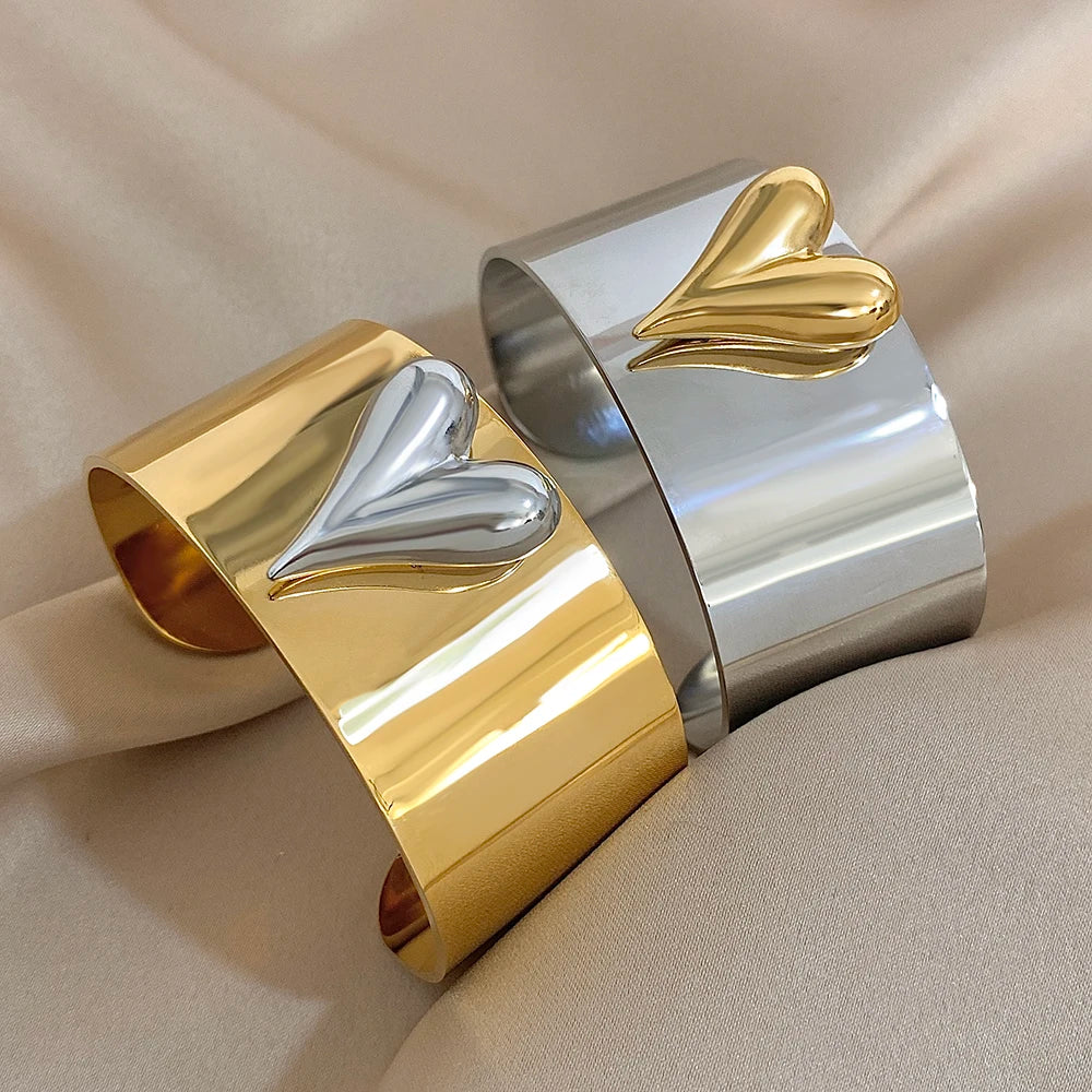 Pair of wide stainless steel cuff bracelets, one gold with a silver heart and one silver with a gold heart.