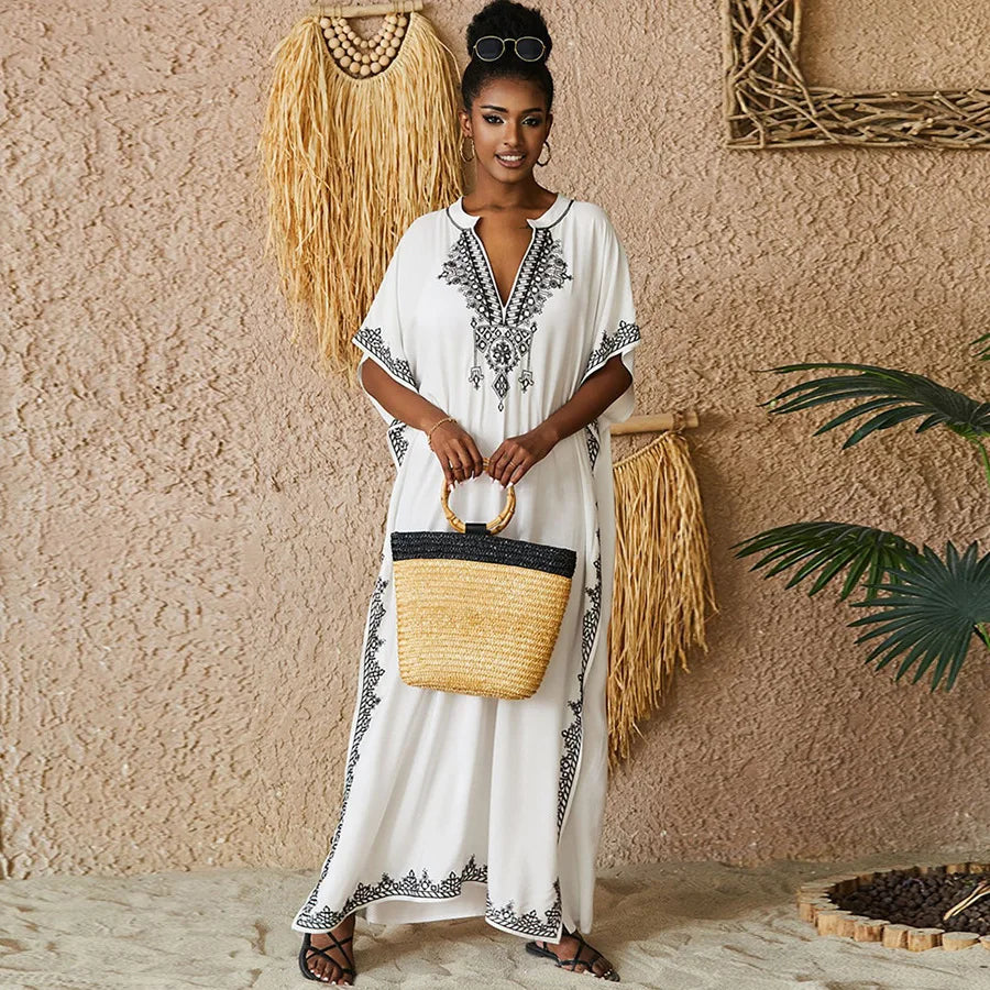 Chic white embroidered kaftan with black patterns, styled with a woven handbag, ideal for beach outings or summer events.