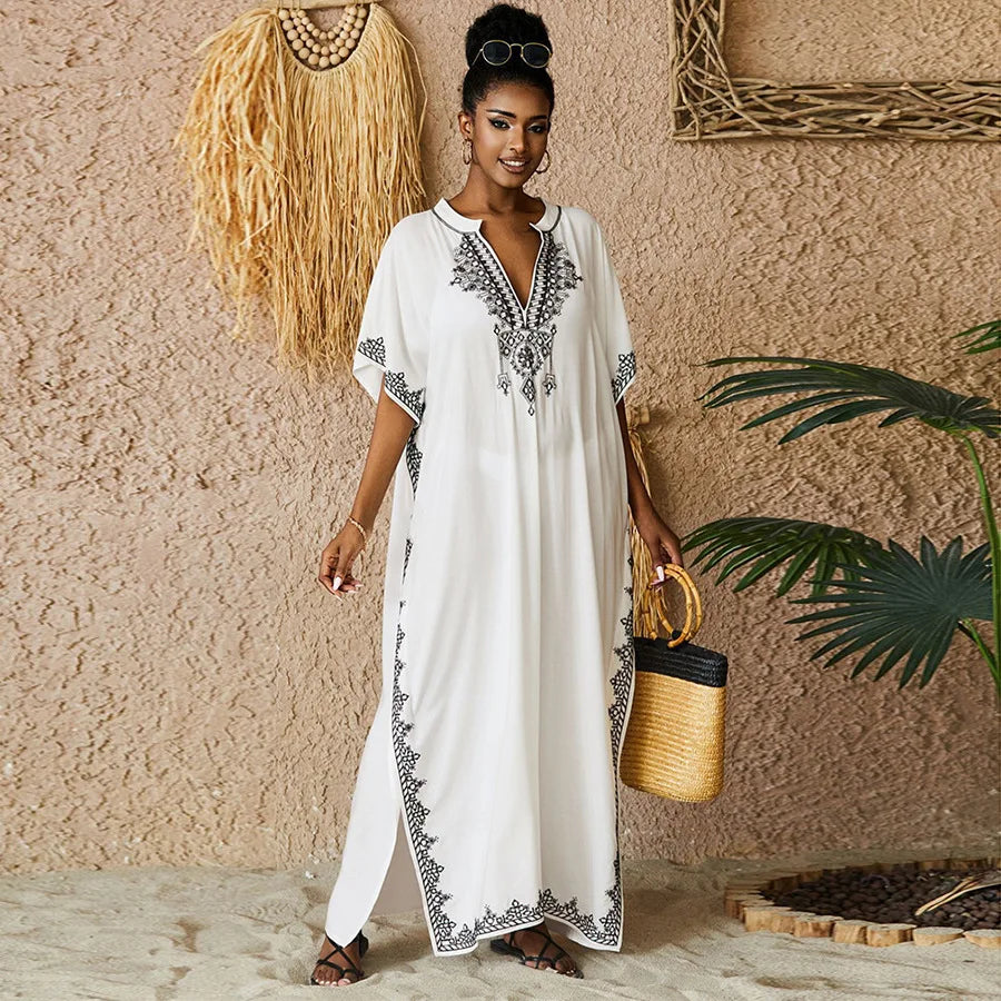 Bohemian-style white embroidered kaftan with black detailing, styled with a straw bag, perfect for beach vacations or summer gatherings.