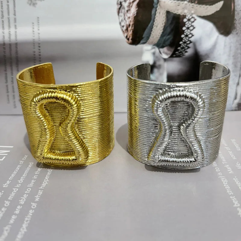 Exaggerated gold and silver keyhole hair cuffs placed side by side on a neutral background.