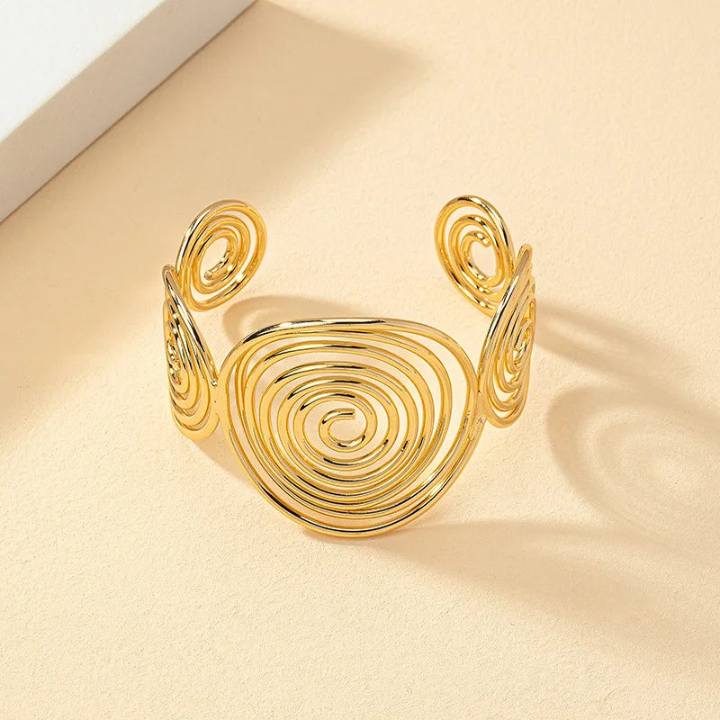 Gold geometric spiral hair cuff with shiny metallic finish, displayed on a beige surface at an angle