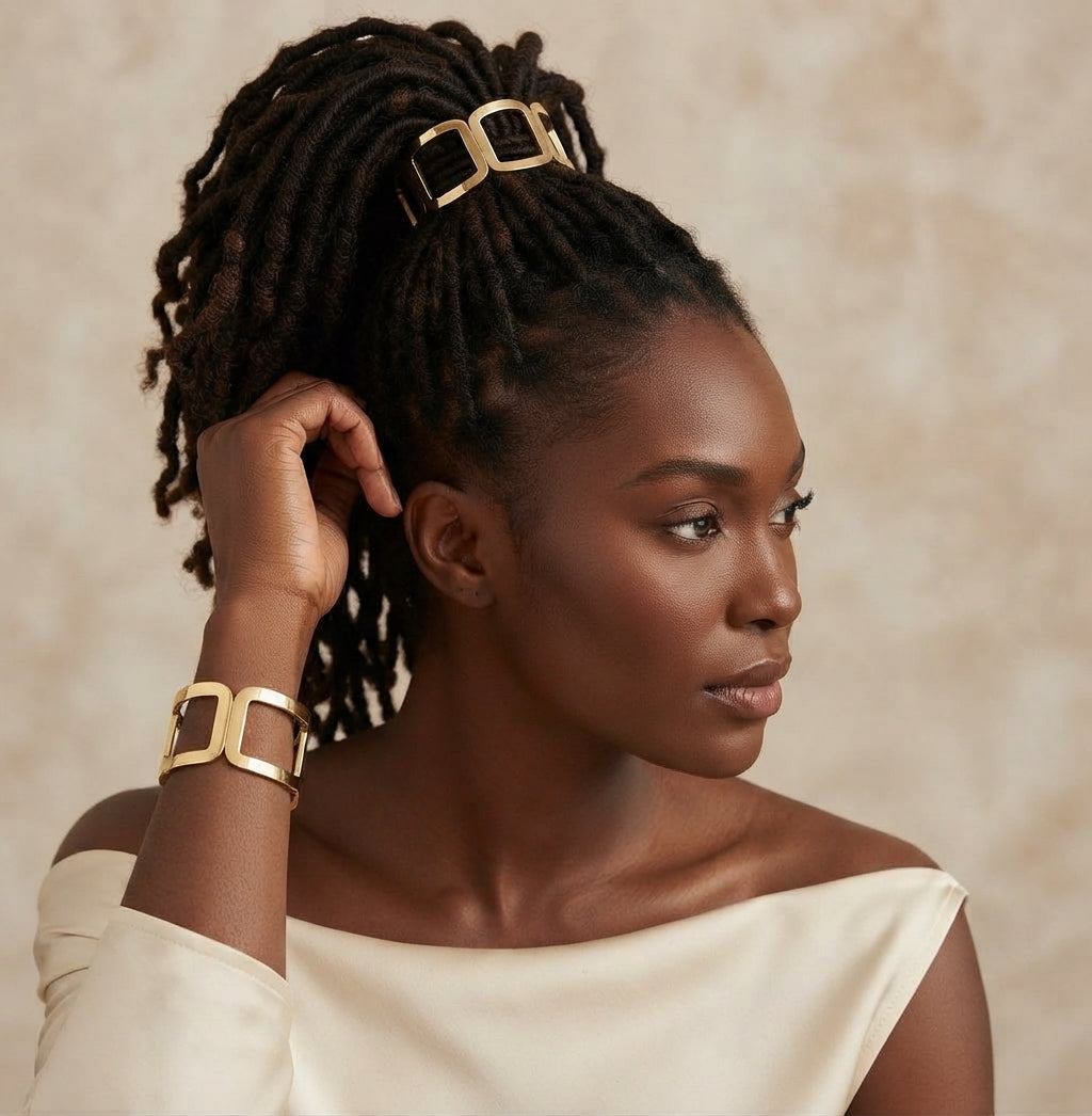 Woman with locs in a high ponytail wearing a gold geometric link hair cuff, with a matching gold cuff on her wrist