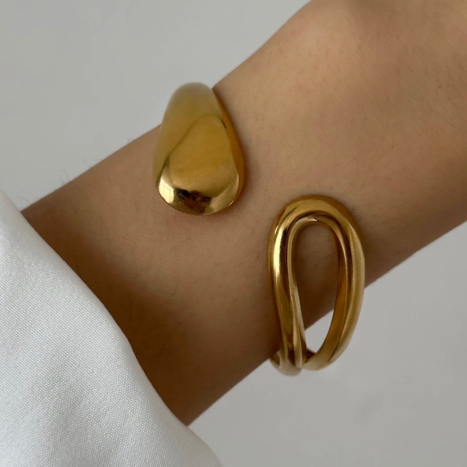 Gold sculptural cuff bracelet featuring one smooth end and one looped end, creating a bold modern statement