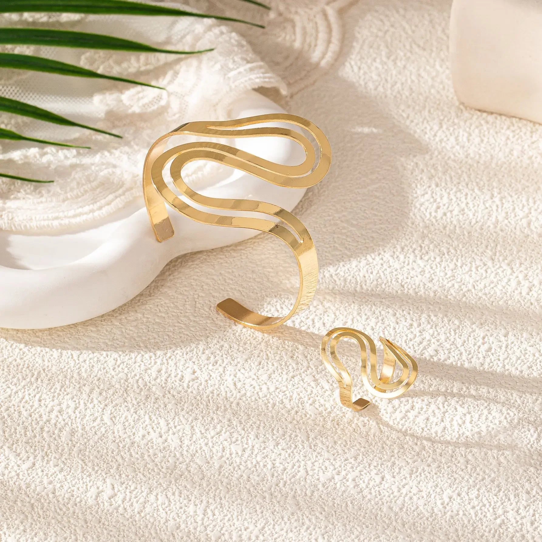Gold snake wave bracelet and matching ring arranged on a textured beige surface, creating an elegant minimalist look