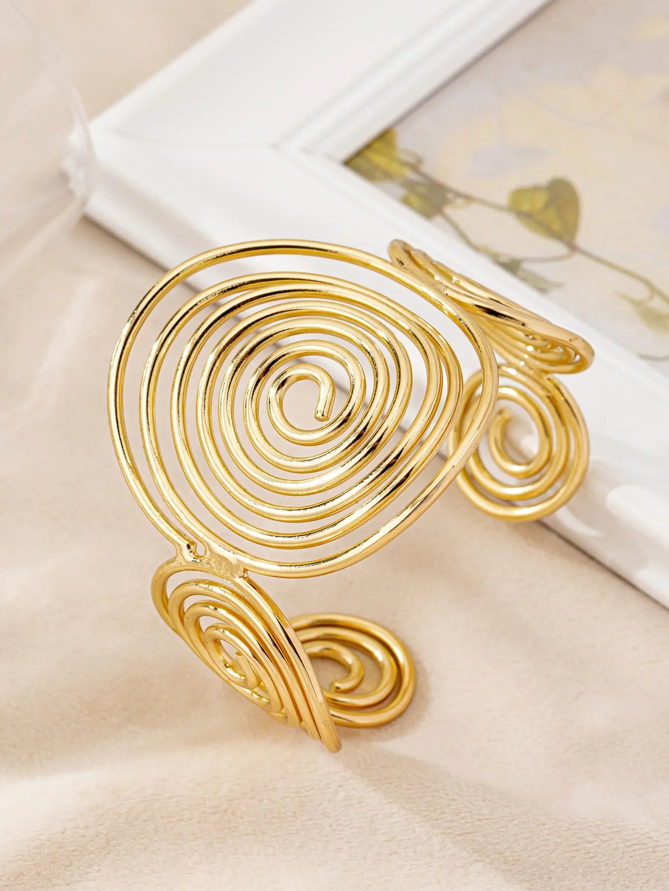 Gold swirl hair cuff with elegant spiral design, displayed on a beige background, front angle.