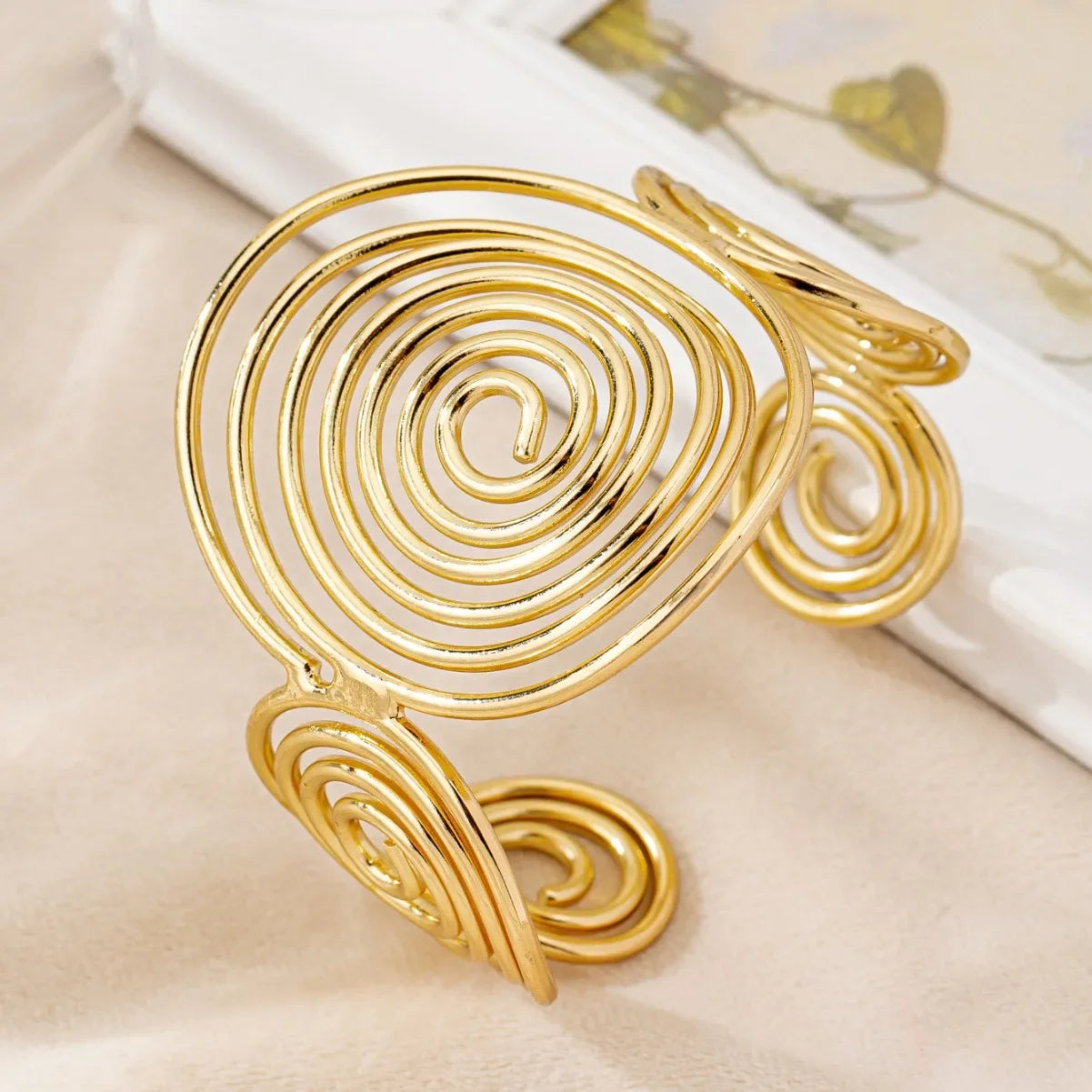 Gold swirl hair cuff with central spiral detail, displayed on a smooth cylinder background.