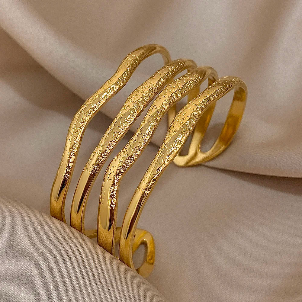 Gold open bracelet with multiple hammered ripple-effect bands displayed on satin fabric