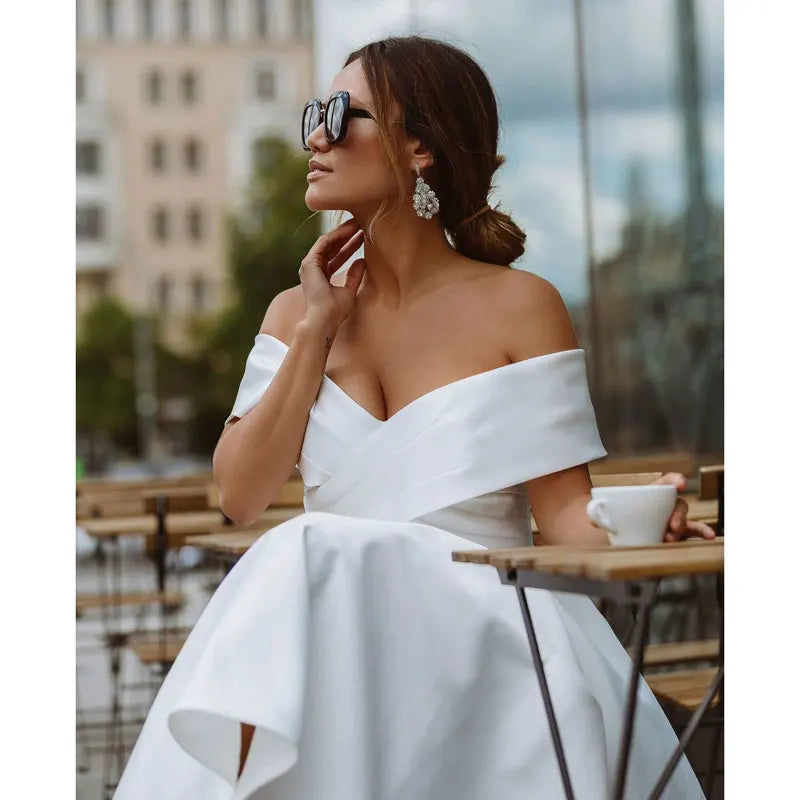Close-up of a woman in an off-shoulder white midi dress, accessorized with statement earrings and sunglasses. A stylish choice for weddings.