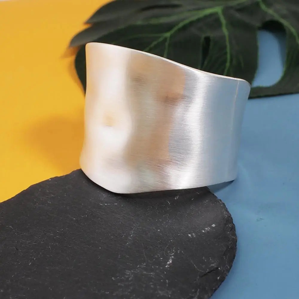 Silver Sunset Gleam Hair Cuff with a wavy, wide cuff design, placed on a slate surface with a tropical leaf in the background.