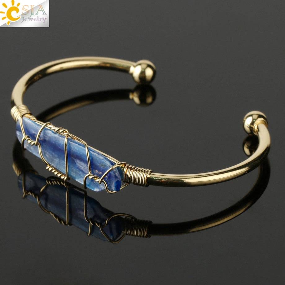 Gold-tone copper bracelet with a wire-wrapped elongated blue crystal quartz centerpiece.