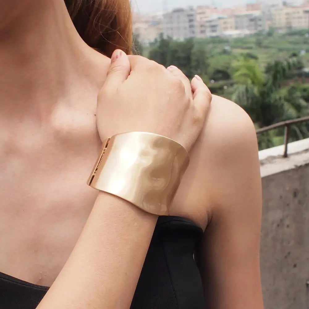Model wearing the gold Sunset Gleam Hair Cuff on her wrist, showcasing its bold and elegant design against an outdoor backdrop.
