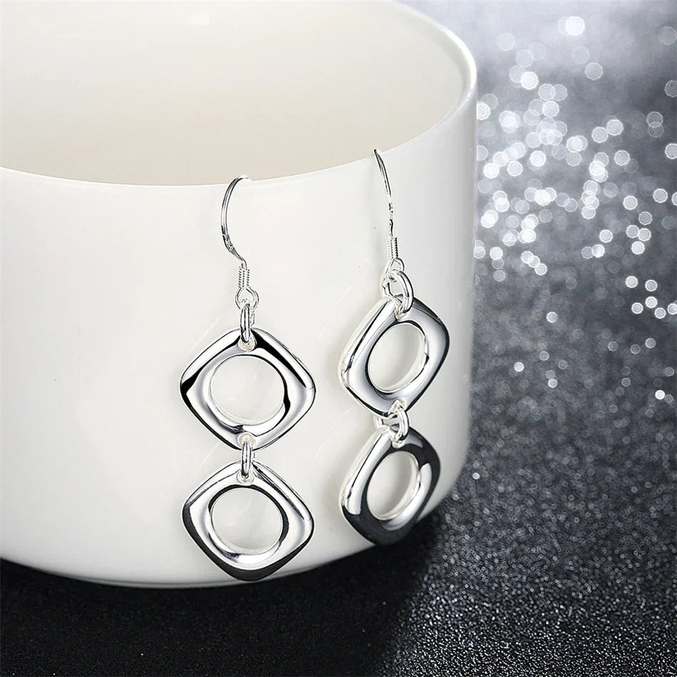 Sterling silver geometric dangle earrings displayed on a white ceramic cup. Minimalist and modern jewelry for timeless style.