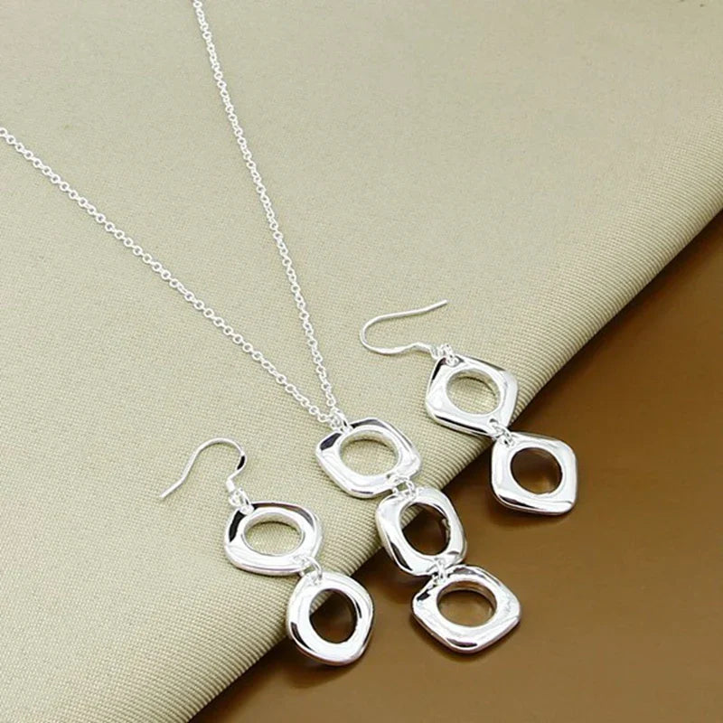 Elegant geometric 925 sterling silver necklace and earrings set displayed on beige fabric. Modern jewelry design perfect for any occasion.