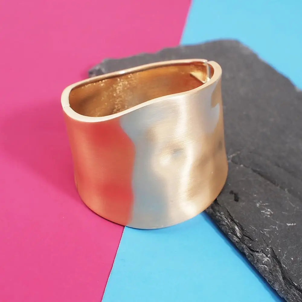 Two-tone Sunset Gleam Hair Cuff in gold and silver, displayed on a slate surface with a vibrant pink and blue background.