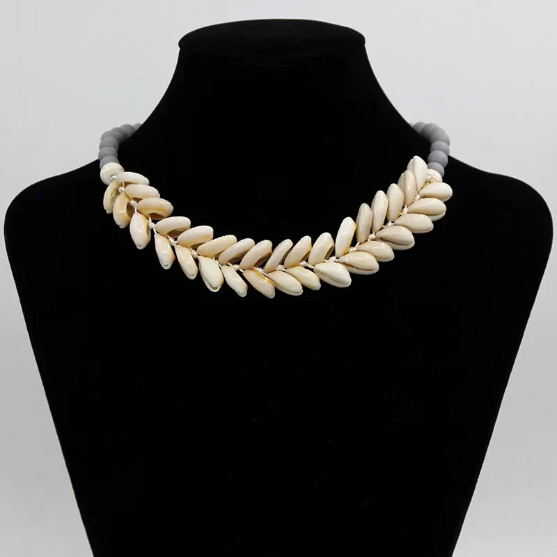 Handmade Cowrie Shell Necklace with gray beads displayed on a black velvet bust. Elegant beach-inspired jewelry for a boho-chic look.