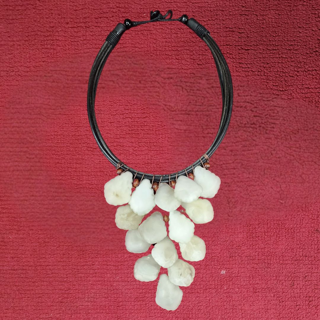 Ivory Petal Cascade Choker displayed against a red fabric background, showcasing its handcrafted white beads and black cord design. A striking statement piece.