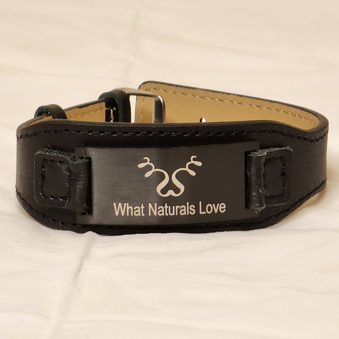 Close-up of the What Naturals Love Hair Tie, a black leather band with an engraved metal plate. Elegant and sturdy hair accessory for locs.