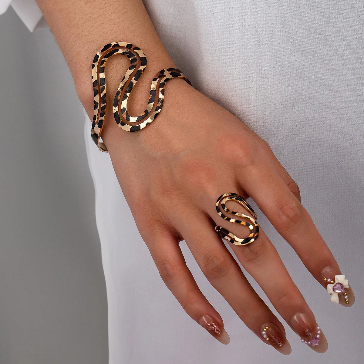 Close-up of a leopard print snake bracelet and matching ring worn on a hand, showcasing a bold and trendy design