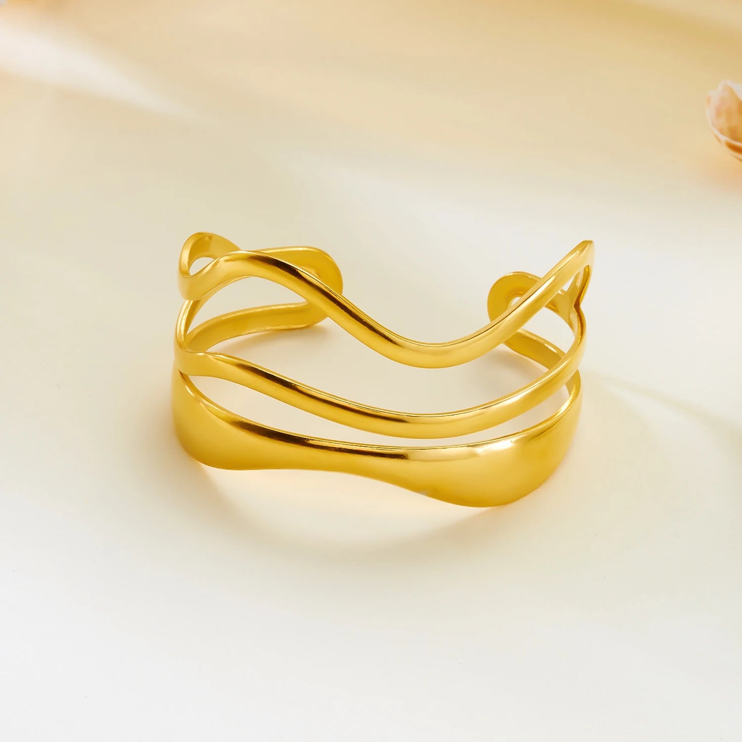 Top view of gold wave cuff bracelet with fluid curved lines and an open bangle design on a soft background