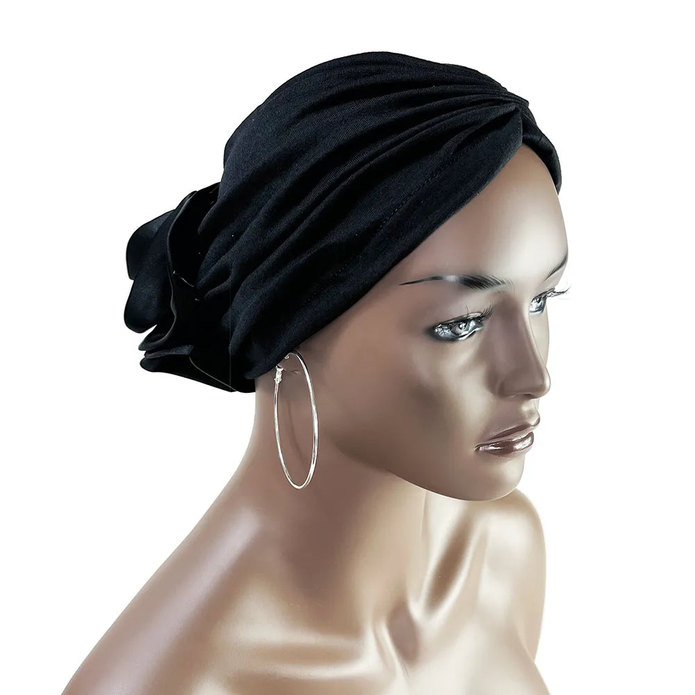 Black floral stretch bandana head wrap worn on a mannequin. Elegant and versatile design with a fabric rose detail at the back.