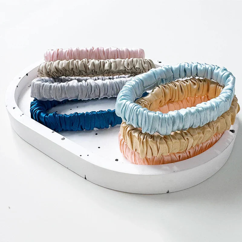 Assorted mulberry silk elastic hair bands in pastel and neutral tones on a white tray. Soft, frizz-free ponytail holders for all hair types.