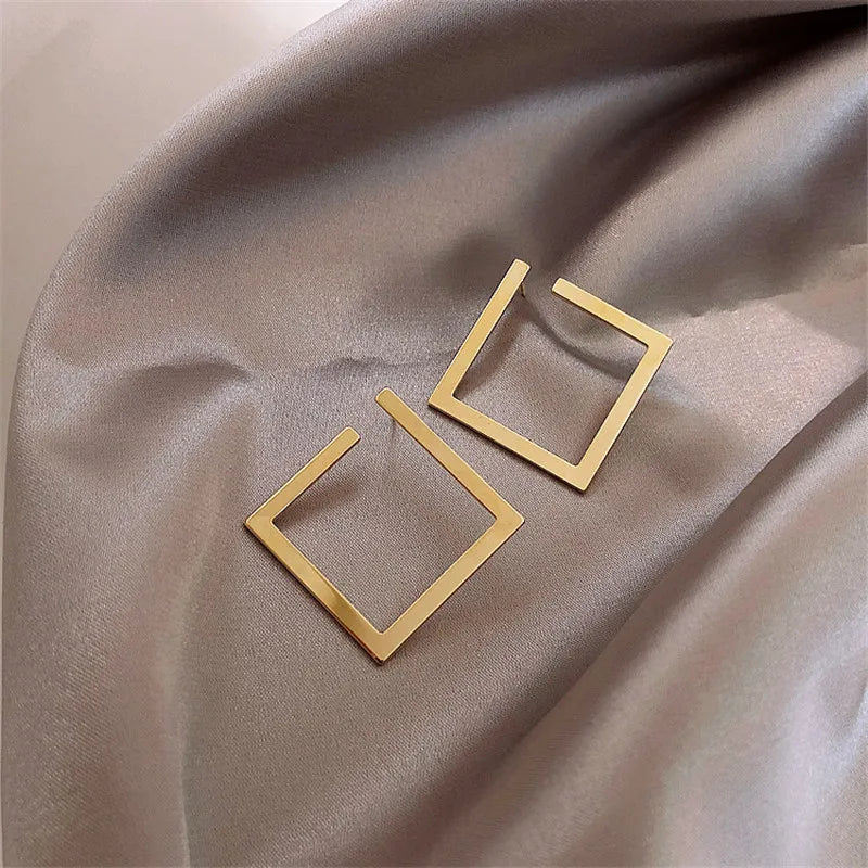 Gold-tone geometric square stud earrings on satin fabric, featuring a modern vintage design. Stylish and elegant earrings for women.
