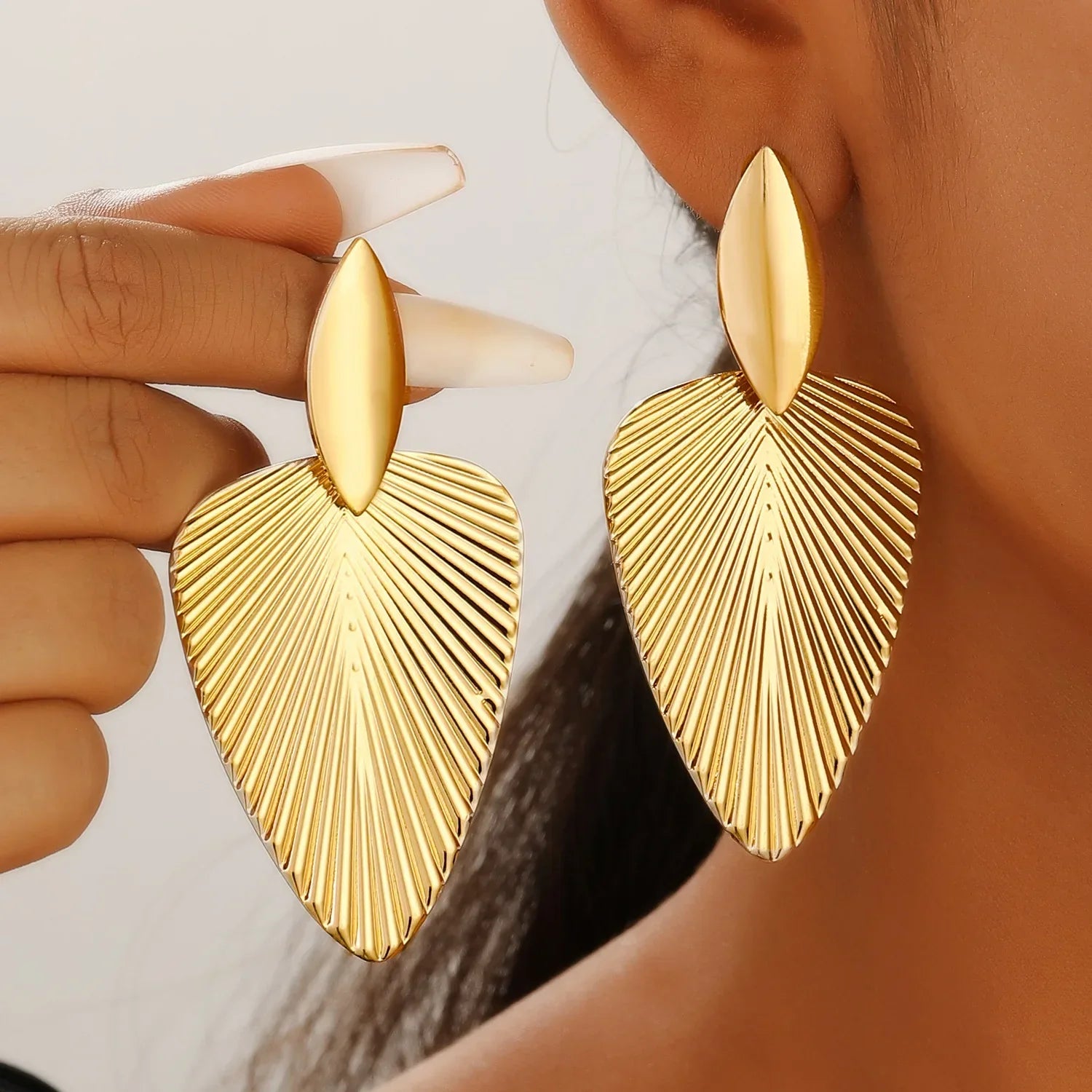 Textured gold fan statement earrings with ribbed detailing, worn by a model for a bold and elegant look. Perfect for chic and vintage-inspired styles.