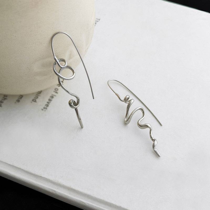 Serenity Threader Earrings in silver displayed on a book, highlighting their intricate three-dimensional design. A stylish and modern jewelry accessory.
