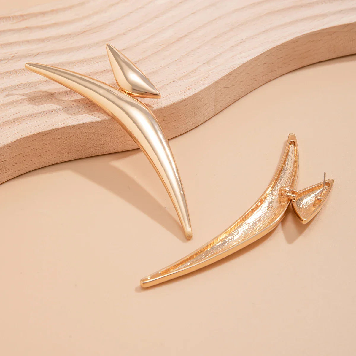 Sleek Aeonian Ear Wings displayed on a wooden surface. Gold-tone geometric earrings with a modern and artistic design.