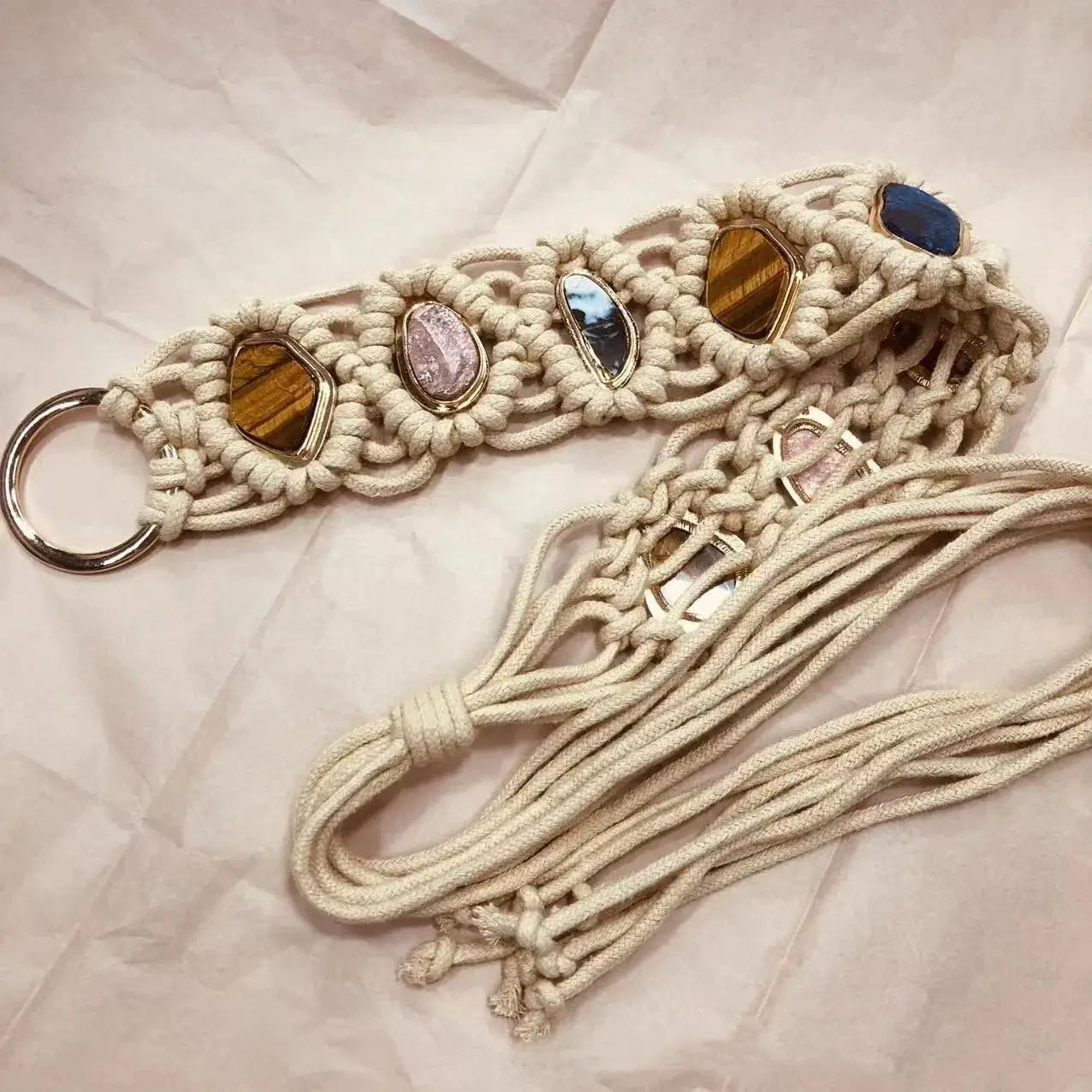 Close-up of a handmade woven tassel belt with braided macramé and gemstone accents. Features a metal ring buckle and long tassel ties for styling.
