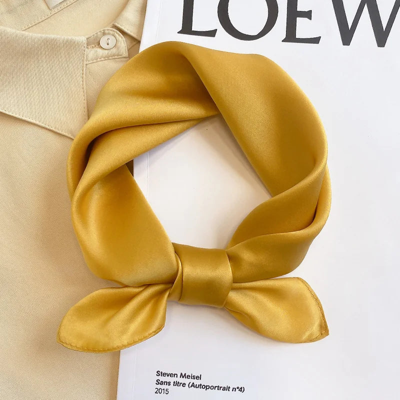 Silk Bandana Scarf - Ivory Elegant displayed in a knotted style on a magazine, showcasing its smooth 100% silk texture and timeless golden hue.