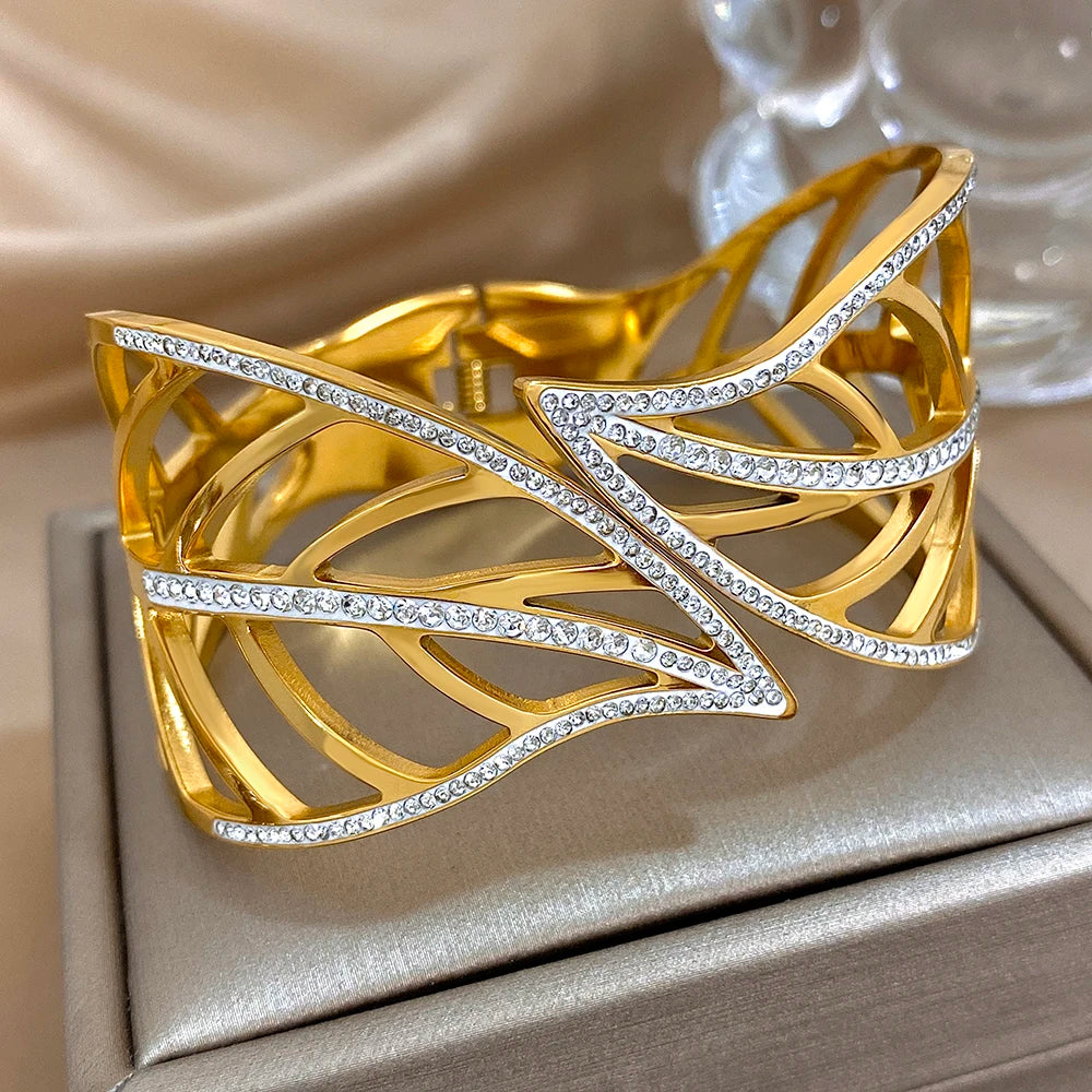 Gold leaf crystal cuff with an openwork design, on a grey display box beside a glass ornament