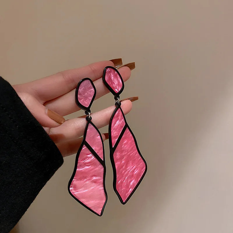 White Oceanic Shard Drop Earrings held in hand. Elegant geometric earrings with a marbled texture, great for sophisticated fashion styles.