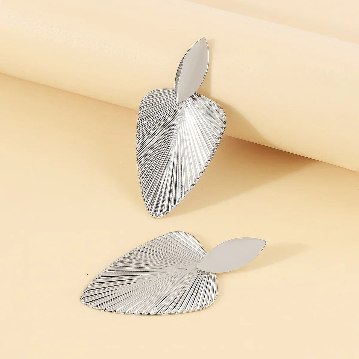Silver fan statement earrings with ribbed detailing displayed on a soft beige background. A stylish and modern accessory for a bold fashion look.