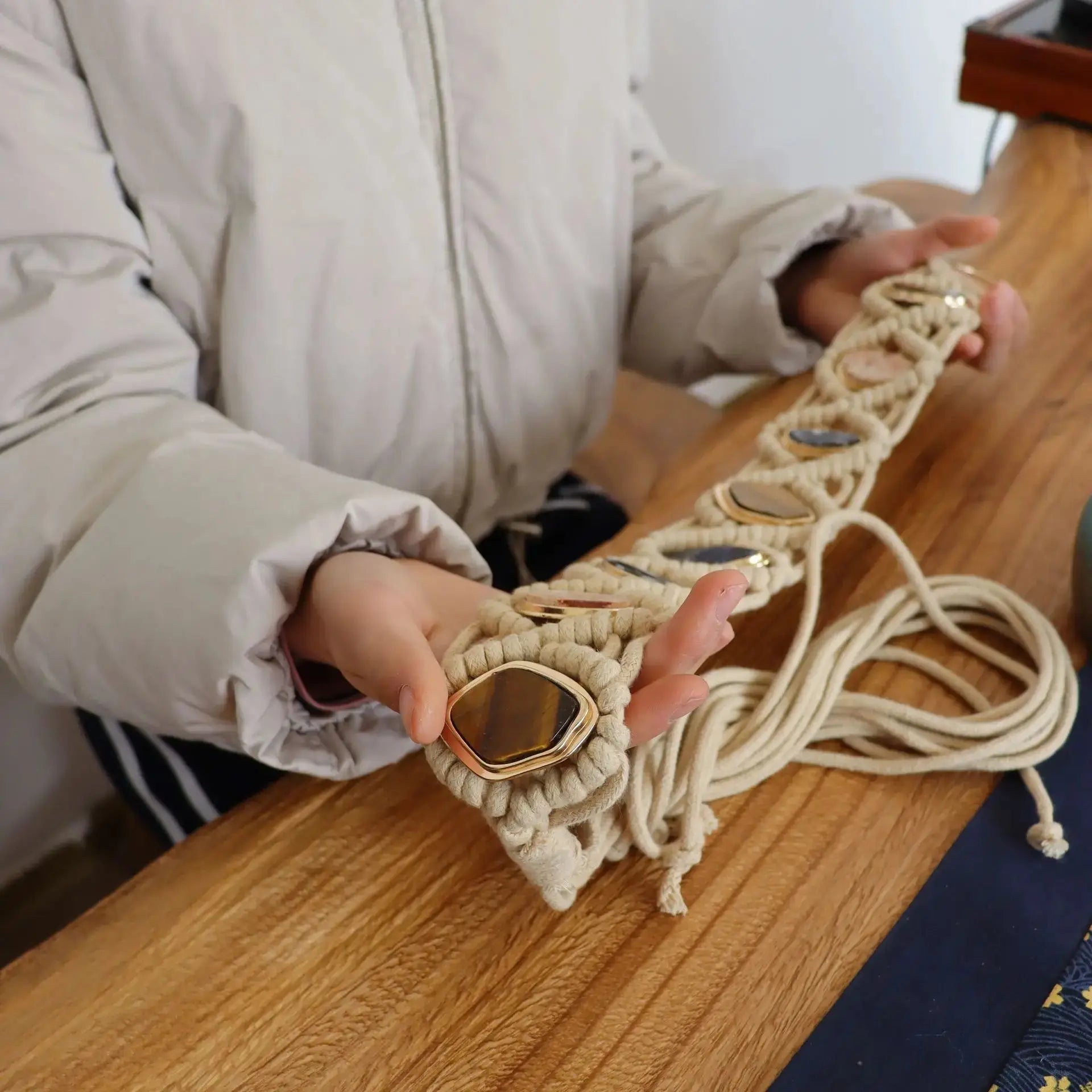 Person holding a handmade woven tassel belt with gemstone details. The intricate macramé design and metal ring closure enhance its boho aesthetic.