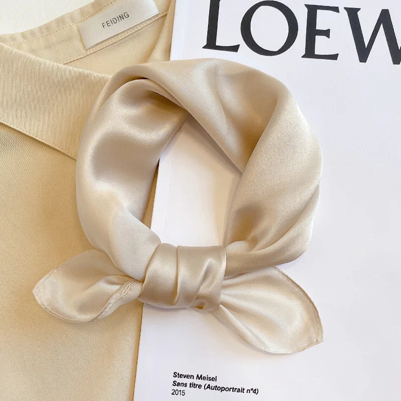 Silk Bandana Scarf - Ivory Elegant tied in a knot on a beige shirt, showcasing its smooth 100% silk texture and timeless hue.