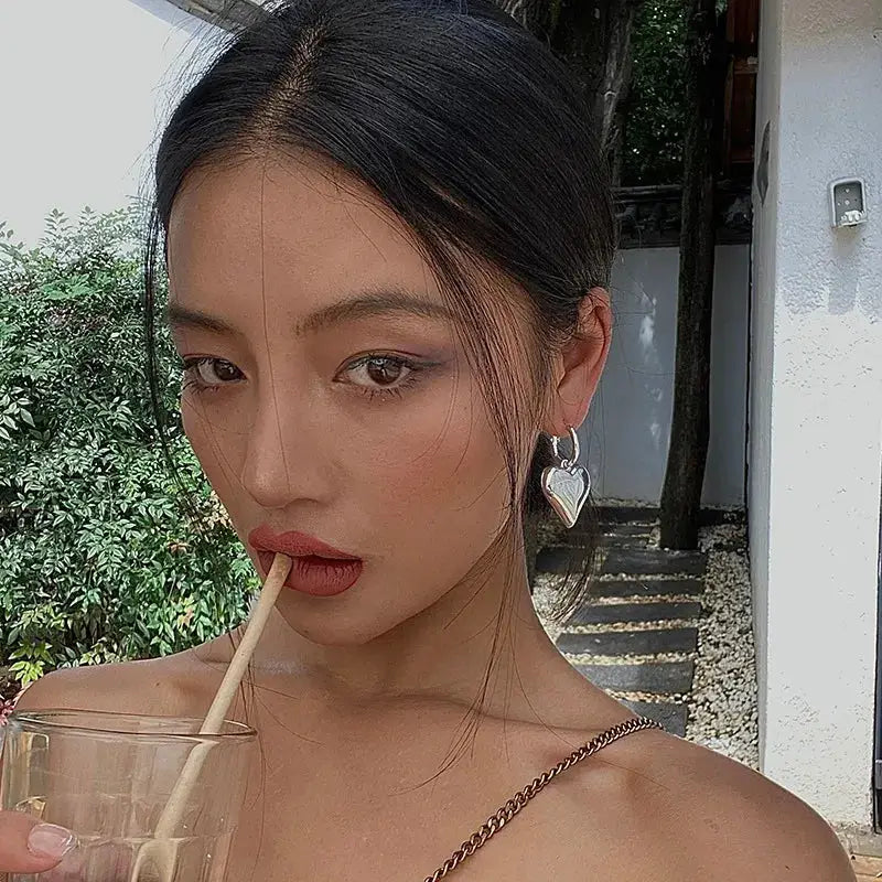 Close-up of a model wearing silver Chic Heart Huggie Hoop Earrings, adding a stylish touch to her outfit.