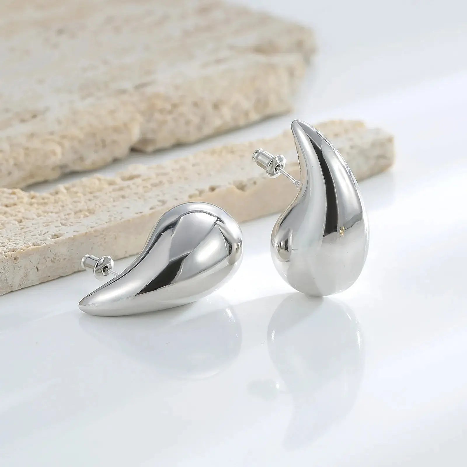Silver teardrop-shaped stud earrings with a polished finish, displayed on a white surface. A modern and elegant accessory.