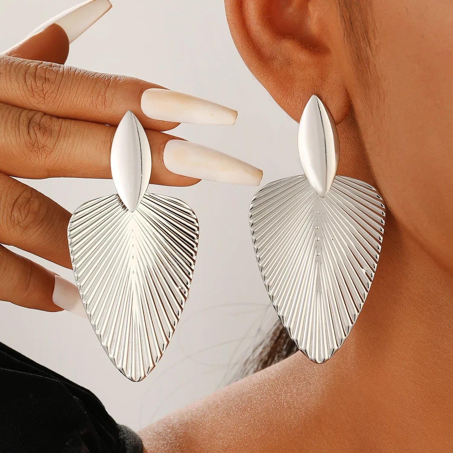 Silver fan statement earrings with ribbed detailing, worn by a model for a bold and elegant look. A chic and modern accessory for any occasion.