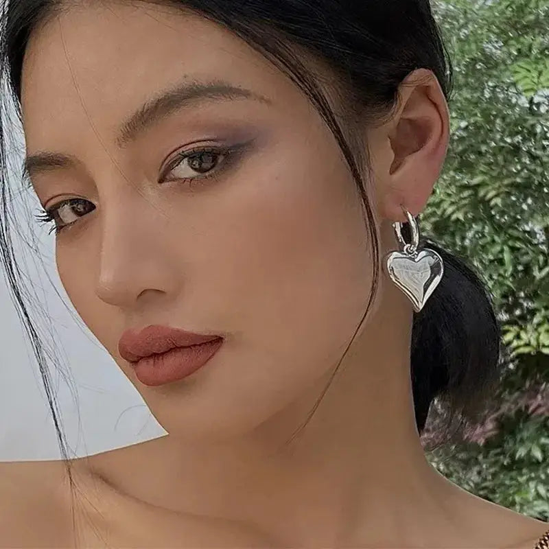 Model showcasing silver Chic Heart Huggie Hoop Earrings with a polished finish. A fashionable and elegant jewelry piece.