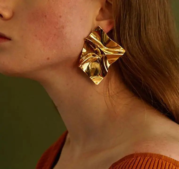 Gold-tone crumpled square stud earrings worn by a model. Bold and stylish modern vintage earrings for women.