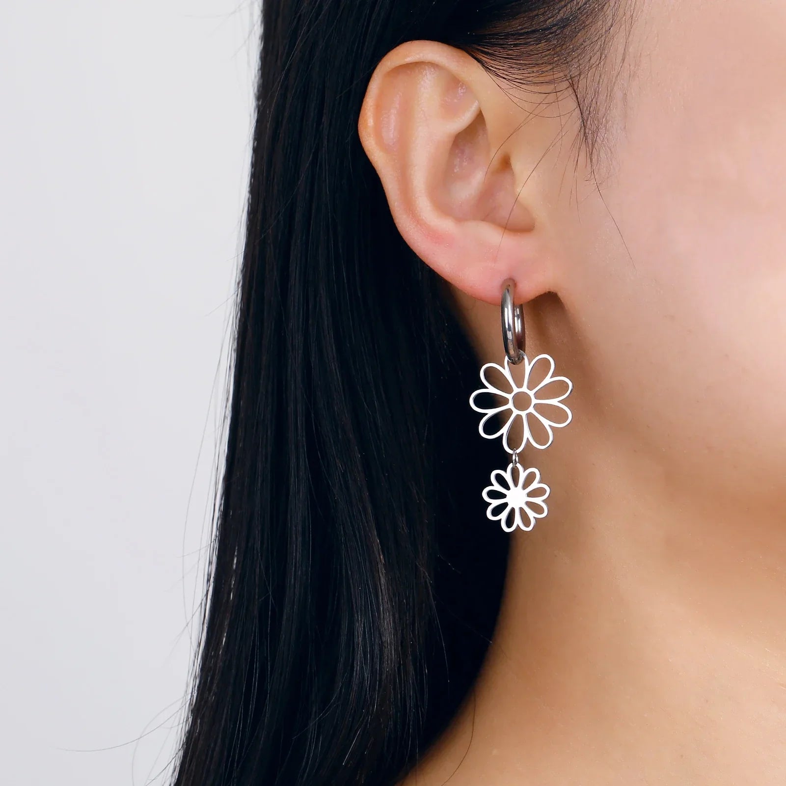 Model wearing silver flower drop earrings with a double floral charm. Lightweight and stylish jewelry for a trendy and elegant look.
