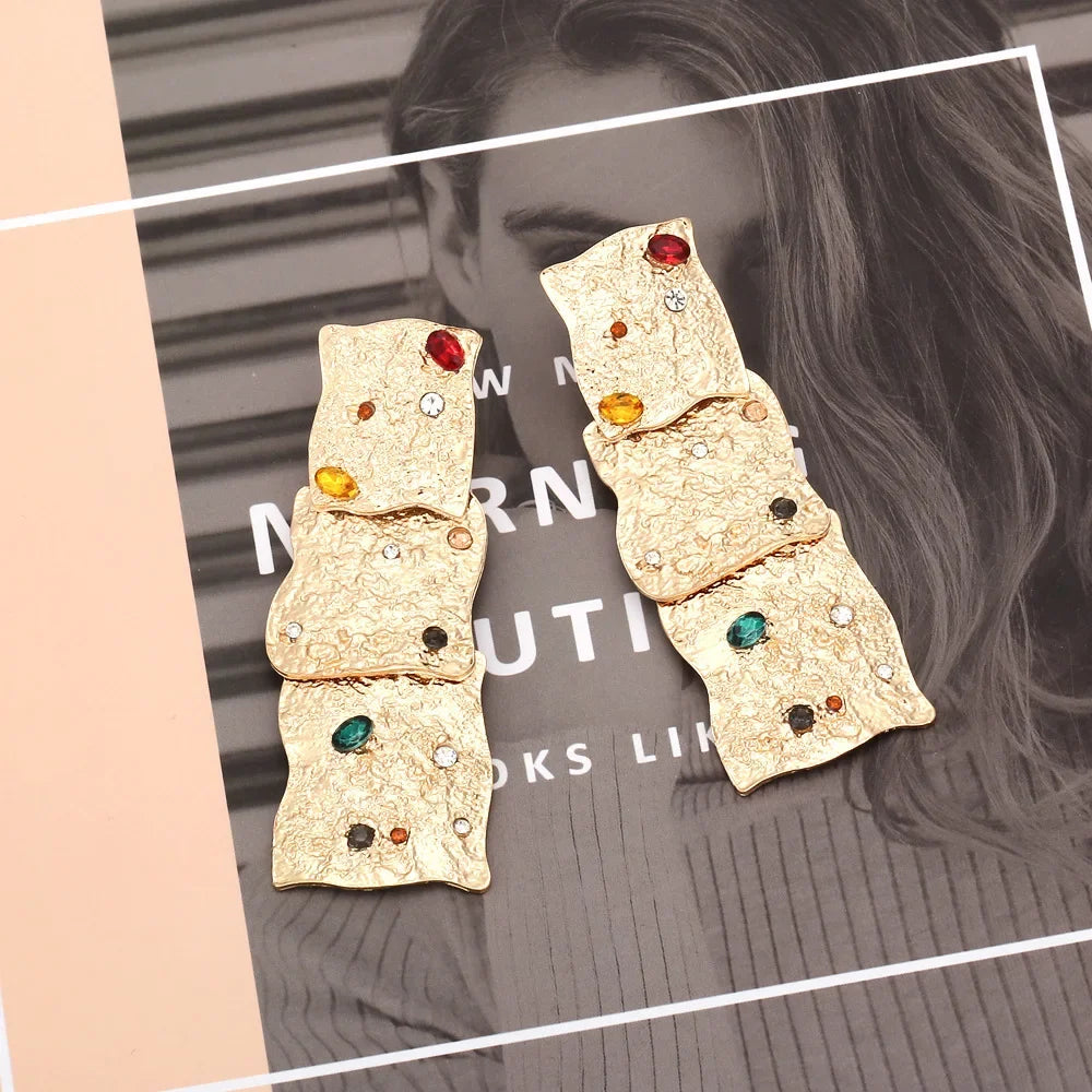 Auric Gemstone Cascade Earrings displayed on a fashion magazine background, highlighting their intricate gold-tone texture and vibrant gemstones.